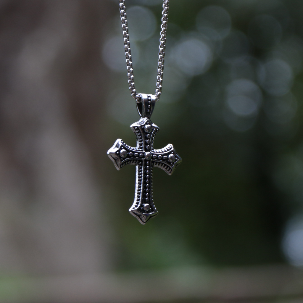 Silver cross pendant on a chain with a blurred natural background