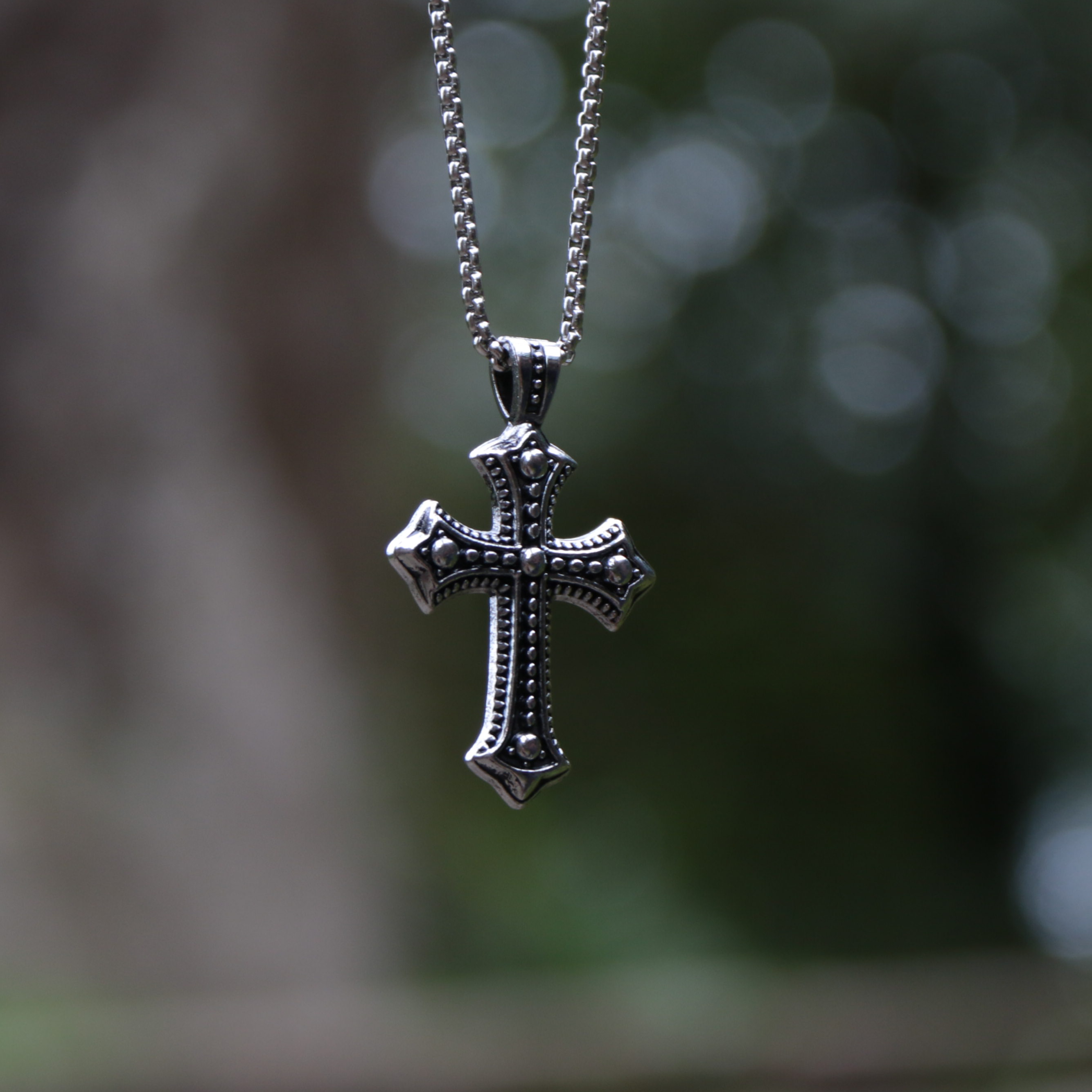 Silver cross pendant on a chain with a blurred natural background